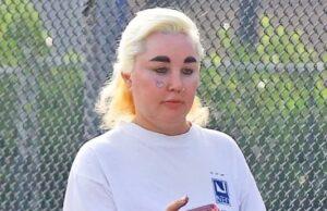 News Room : Amanda Bynes unveils latest body modification after getting lip fillers and dropping almost 30lbs on Ozempic Woman using smartphone outdoors near a fence with greenery in the background.