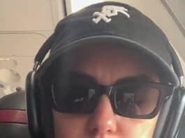 Sunglasses-wearing woman with headset on airplane, casual attire, serious expression.