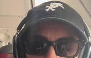 Sunglasses-wearing woman with headset on airplane, casual attire, serious expression.