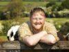 News Room : Clarkson’s Farm star Kaleb Cooper’s staggering earnings are revealed as he shares the dream way he wants to spend the money Happy man smiling outdoors with cows and green fields in background.