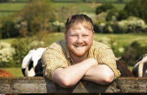 Happy man smiling outdoors with cows and green fields in background.