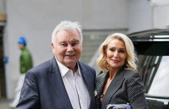 News Room : Eamonn Holmes, 66, ‘purchases new pad for him to enjoy cosy weekends away with girlfriend Katie Alexander’, 44, amid divorce from Ruth Langsford Elderly man with walker and woman in formal attire smiling outdoors.
