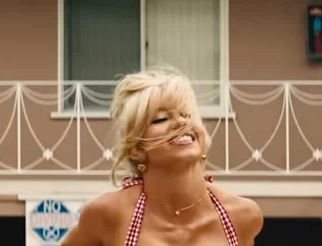 Blonde woman smiling in a red checkered bikini, outdoors, sunny weather.