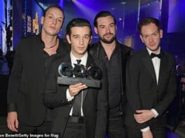 Men in formal suits accepting an award at a ceremony in a nightclub or event hall.