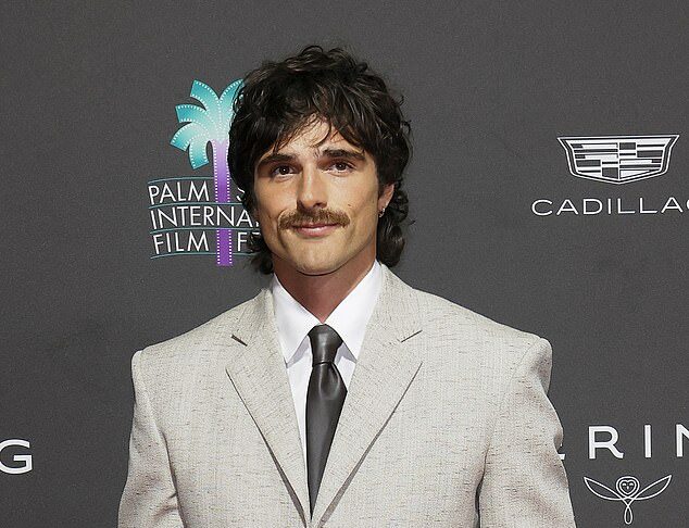 Stylish man in a light gray suit at a film festival event with Palm Springs International Film Festival logo in the background.