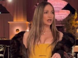 Elegant woman in a yellow dress and fur jacket at a glamorous event, holding a handbag and sunglasses.