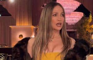 Elegant woman in a yellow dress and fur jacket at a glamorous event, holding a handbag and sunglasses.