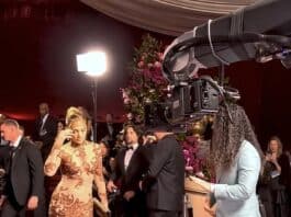 Elegant woman in glamorous gown being filmed at red carpet event with professional camera crew.