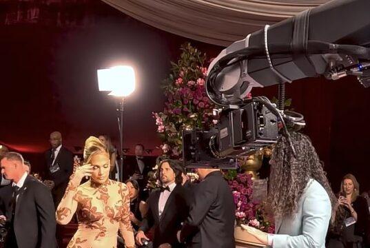 Elegant woman in glamorous gown being filmed at red carpet event with professional camera crew.