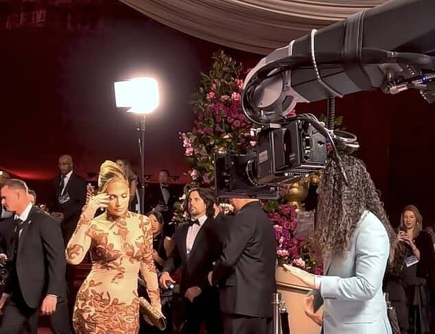 Elegant woman in glamorous gown being filmed at red carpet event with professional camera crew.
