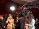 Elegant woman in glamorous gown being filmed at red carpet event with professional camera crew.