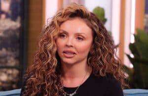 Curly-haired woman speaking passionately on a talk show set.