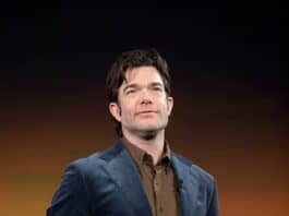 Man in navy blazer on stage at a conference or event in front of a colorful background.