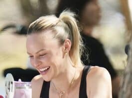 Smiling woman enjoying a meal at an outdoor cafe, wearing black top and gold jewelry.