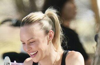 Smiling woman enjoying a meal at an outdoor cafe, wearing black top and gold jewelry.