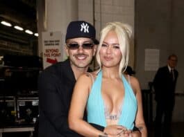 Smiling couple embracing at an indoor event, woman in a striking blue gown with thigh-high slit.