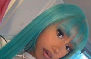 Vibrant turquoise-haired woman with jewelry and bold makeup in a modern room setting.