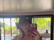Vibrant woman in polka dot swimsuit and cowboy hat taking mirror selfie indoors at bright, modern space.