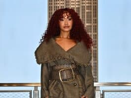 Stylish woman in a textured coat, patterned tights, and fur boots on city rooftop balcony at sunset.