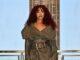 News Room : Leigh-Anne Pinnock is funding her debut solo album out of her own pocket after claiming her former record label ‘doesn’t have the budget’ Stylish woman in a textured coat, patterned tights, and fur boots on city rooftop balcony at sunset.