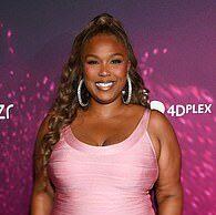 Smiling woman in pink dress at Lanka News Room event with vibrant purple backdrop.