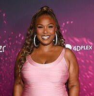 Smiling woman in pink dress at Lanka News Room event with vibrant purple backdrop.