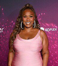 Smiling woman in pink dress at Lanka News Room event with vibrant purple backdrop.