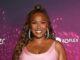 News Room : Lizzo shows off incredible weight loss in skintight dress as she joins Demi Lovato and Sofia Vergara at premiere of Paris Hilton’s Infinite Icon documentary Smiling woman in pink dress at Lanka News Room event with vibrant purple backdrop.