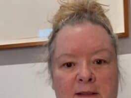 Uncertain woman with messy hair in casual grey shirt indoors, plain wall background.