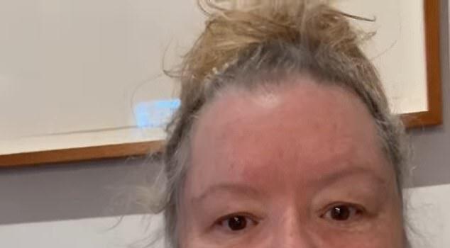 Uncertain woman with messy hair in casual grey shirt indoors, plain wall background.