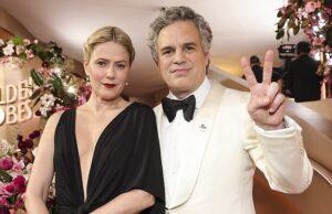 Elegant couple at a glamorous event, dressed in formal attire with floral decor in the background.