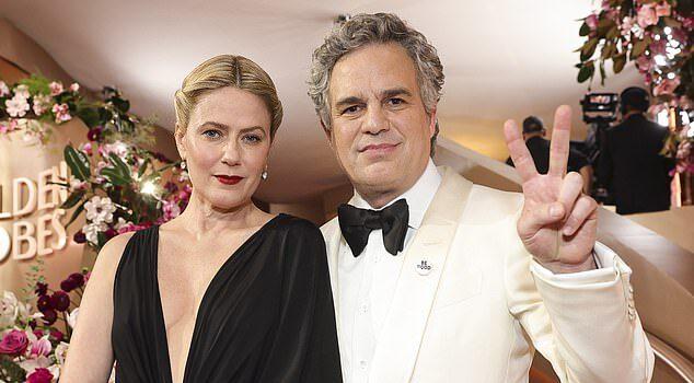 Elegant couple at a glamorous event, dressed in formal attire with floral decor in the background.