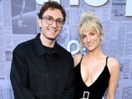 Smart man and woman posing for photo at media event in front of newspaper backdrop.