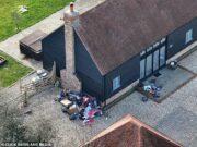 Overflowing trash piles outside black wooden house in a residential area.