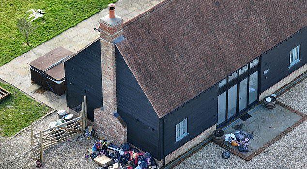 Overflowing trash piles outside black wooden house in a residential area.