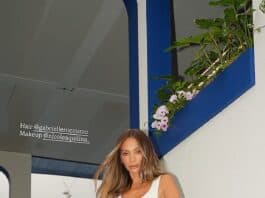 Stylish woman on staircase wearing white outfit with hair and makeup details provided.