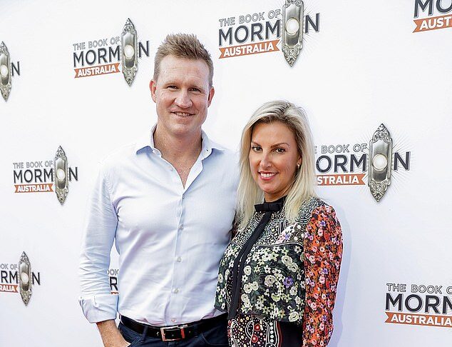 Elegant man and woman at book launch event for "The Book of Mormons Australia" in front of branded backdrop, red carpet, stylish attire, smiling, event photos.