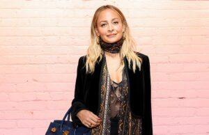 Fashionable woman with blonde hair posing against a pink brick wall, holding a blue handbag.