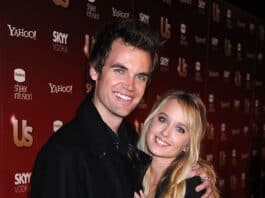 Smiling young couple at entertainment event, standing close together in front of media backdrop.