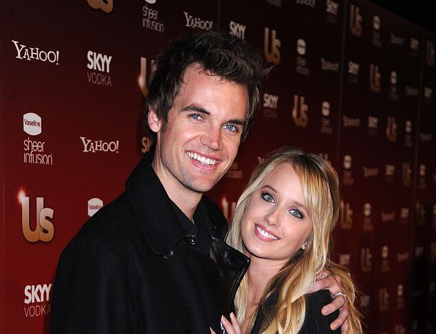 Smiling young couple at entertainment event, standing close together in front of media backdrop.
