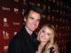News Room : One Tree Hill star Tyler Hilton and actress wife Megan Park split after 10 years of marriage Smiling young couple at entertainment event, standing close together in front of media backdrop.