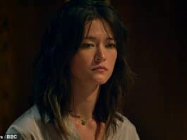 Young woman with dark wavy hair, contemplative expression, indoor dark background.