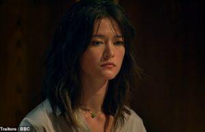 Young woman with dark wavy hair, contemplative expression, indoor dark background.