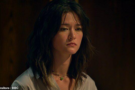 Young woman with dark wavy hair, contemplative expression, indoor dark background.