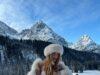 Hot woman in winter landscape in bikini and fur hat, snowy mountains in background, scenic outdoor photo.