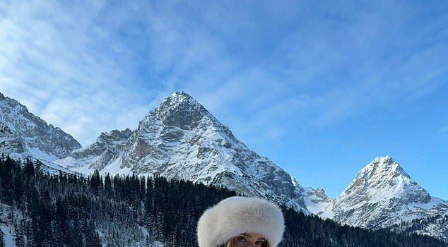 Hot woman in winter landscape in bikini and fur hat, snowy mountains in background, scenic outdoor photo.