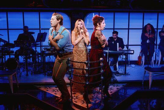 Performers on stage during a theatrical show in a vibrant, modern setting with live musicians in the background.