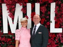 Elegant woman in pink dress with hat, standing with man in dark suit at floral backdrop event.