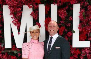 Elegant woman in pink dress with hat, standing with man in dark suit at floral backdrop event.